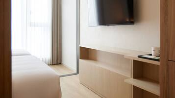 A hotel room with a bed, a mounted TV, wooden shelves, and a window with curtains.