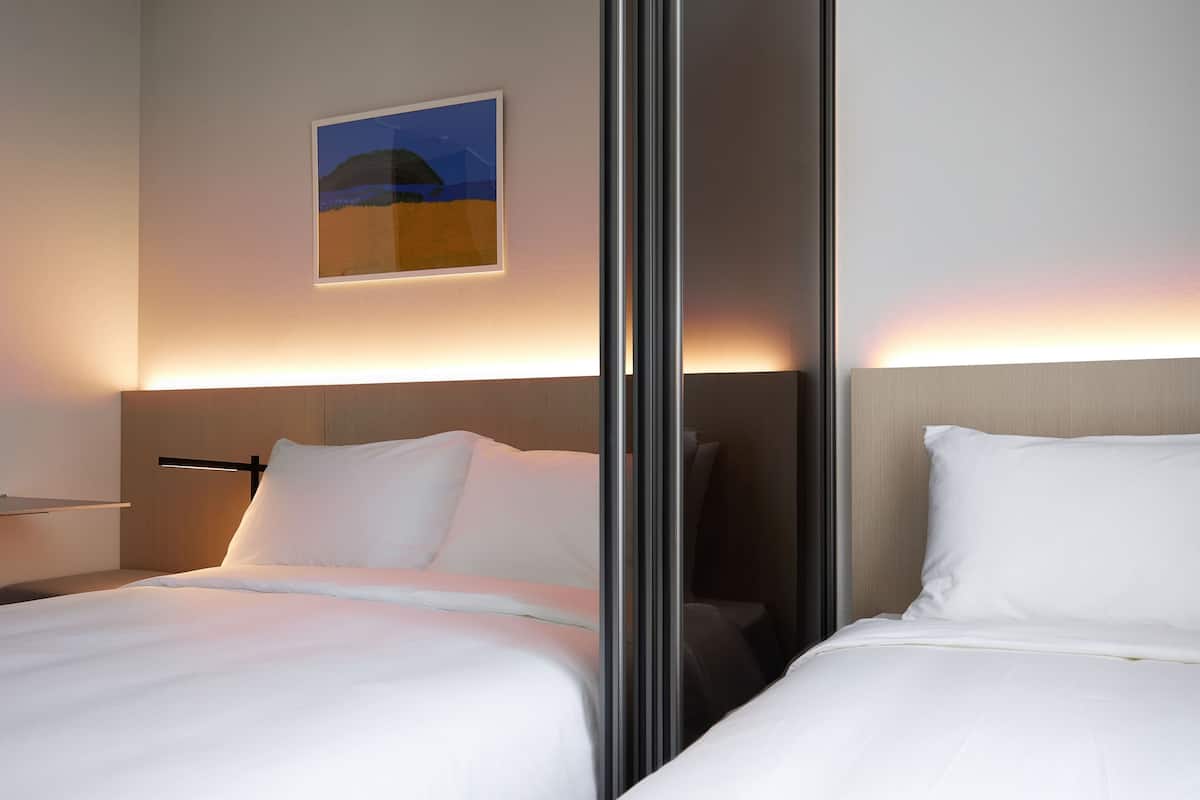 A hotel room with two beds, a nightstand, and a wall-mounted artwork.