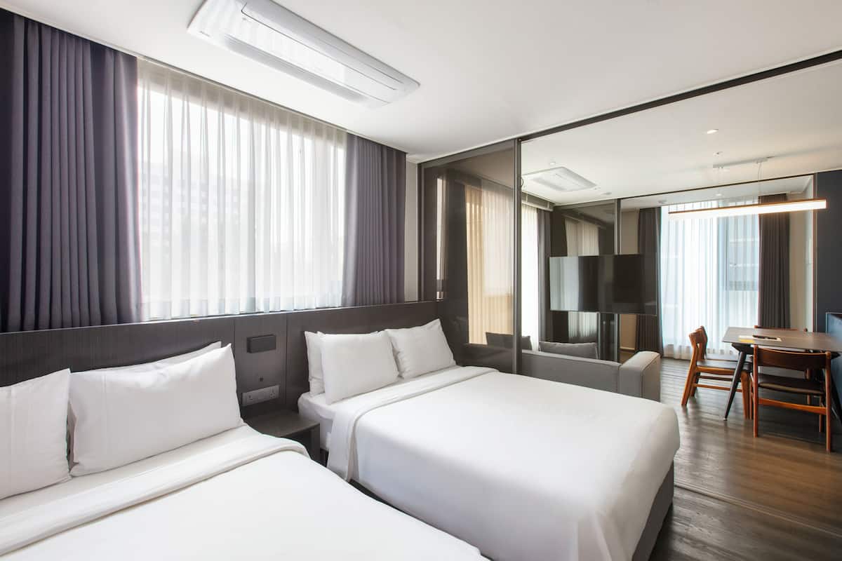 A hotel room with two beds, a desk, a chair, a TV, and a large mirror.