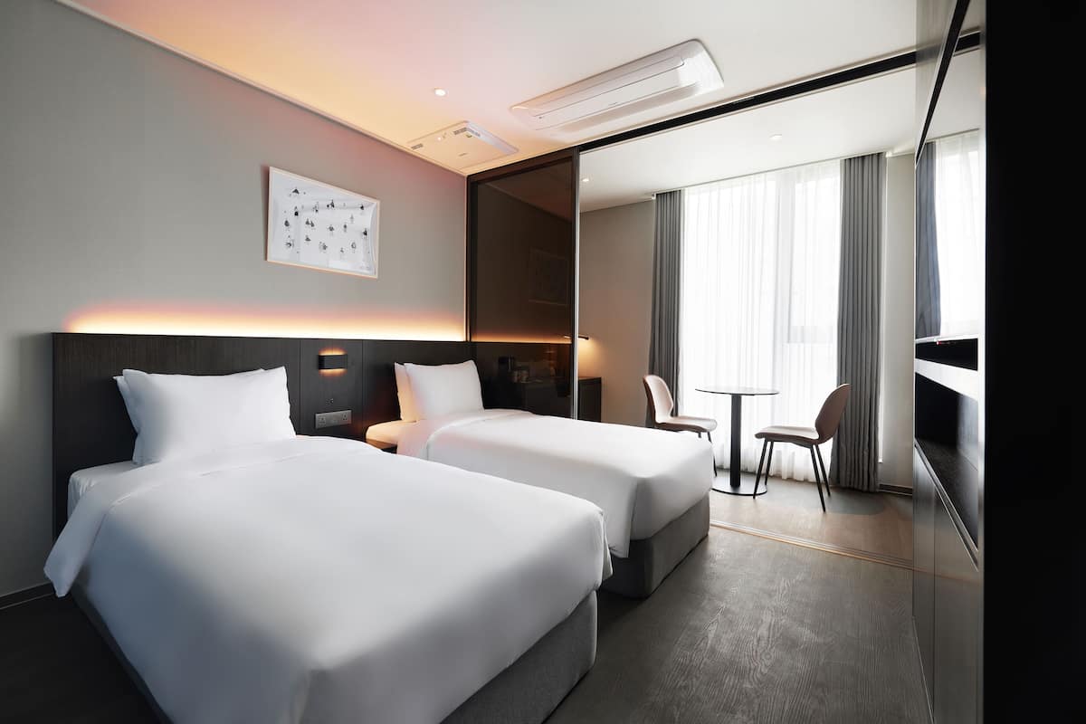 A hotel room with two beds, a desk, a chair, and a large window with curtains.