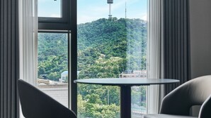 Una habitación moderna con un ventanal grande que da a una colina verde y una torre. Hay una mesa redonda con dos sillas.