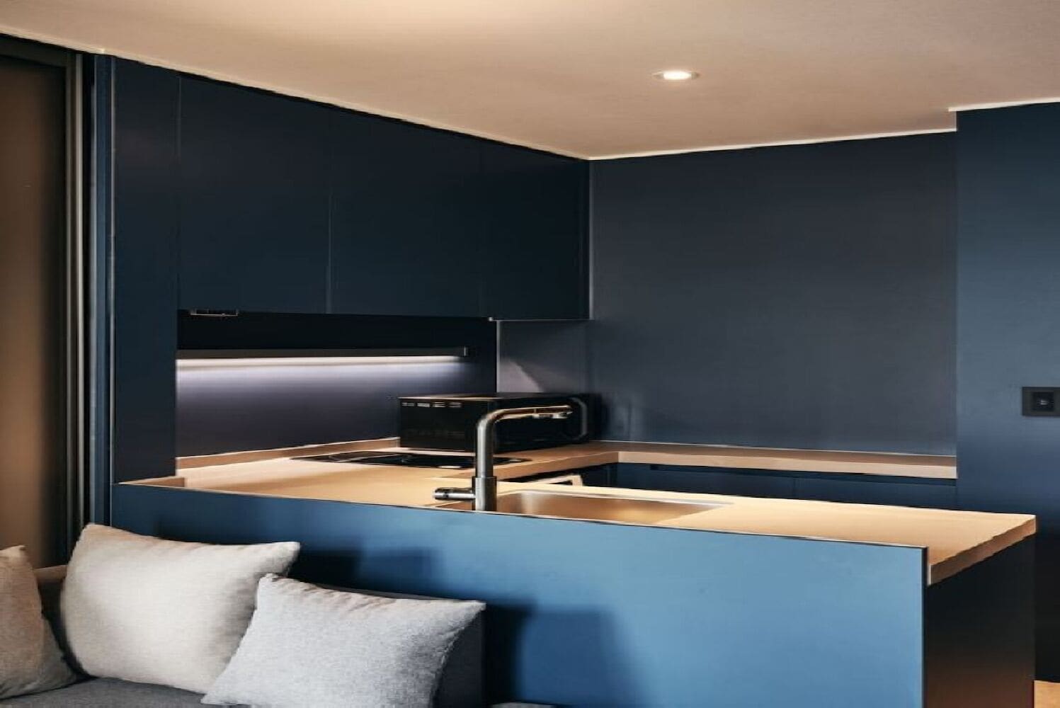 Une cuisine moderne avec des meubles de couleur bleu foncé, un four encastré et un plan de travail doté d’un évier.