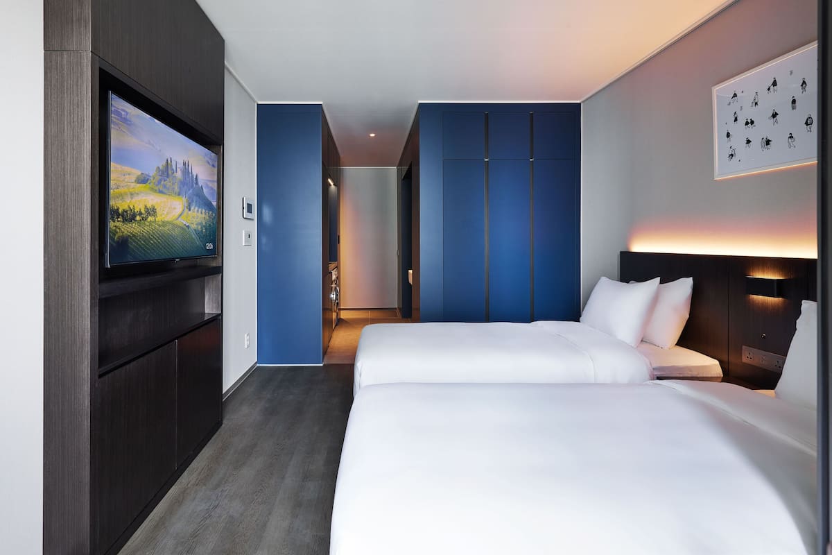 A modern hotel room with a large flat-screen TV, a neatly made bed, and a blue accent wall.