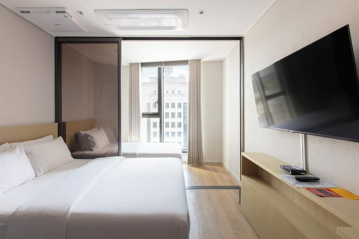 A hotel room with a large bed, a flat-screen TV, a desk with a chair, and a window with curtains.