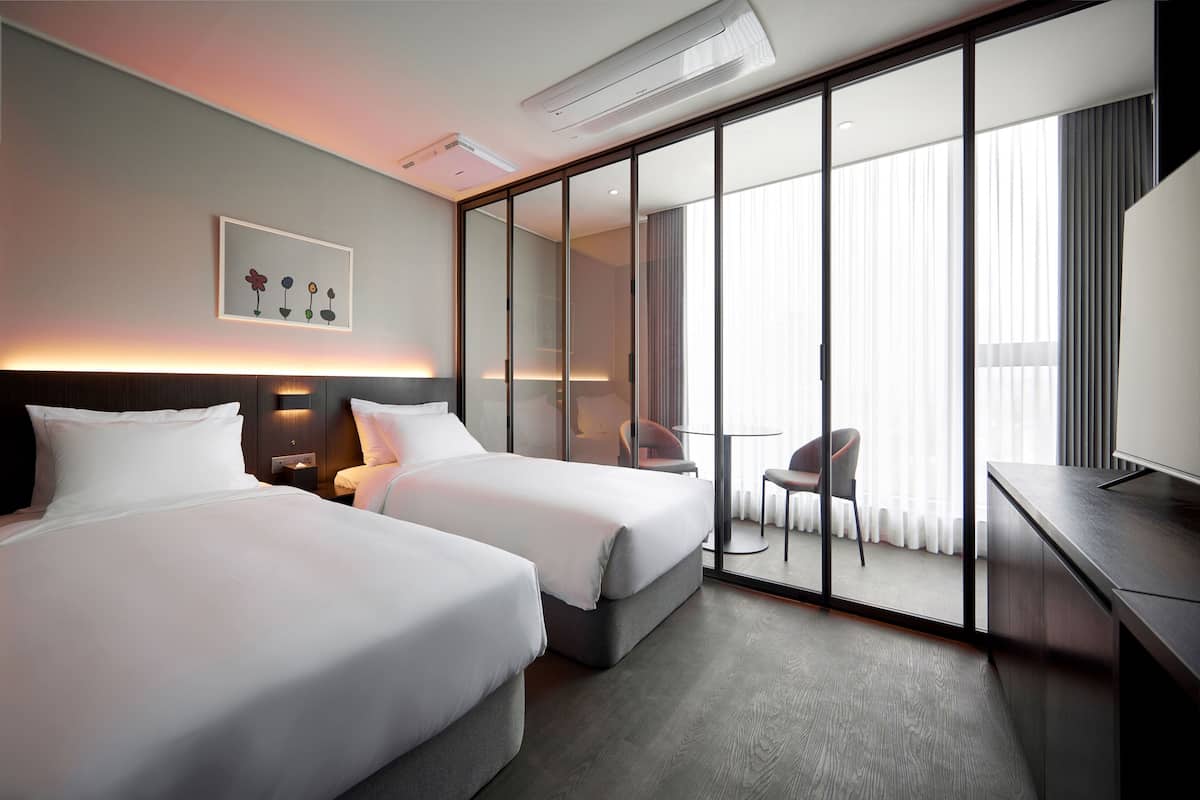 A hotel room with two beds, a desk, a chair, and a large window with curtains.