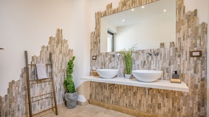 A bathroom with a stone mosaic wall, two sinks, a large mirror, and a ladder.