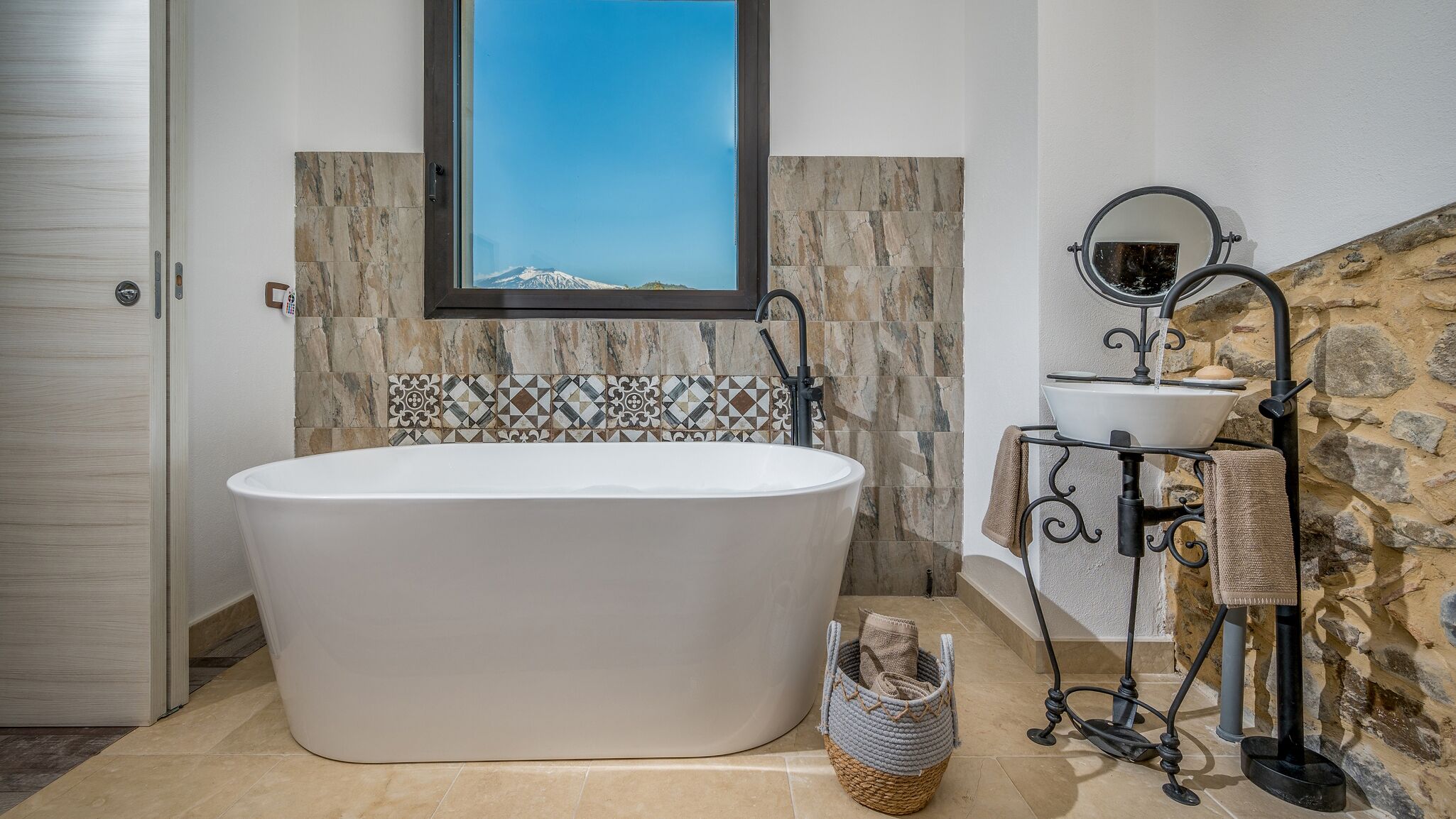 Ein modernes Badezimmer mit freistehender Badewanne, Waschbecken mit Spiegel und einer Steinwand.