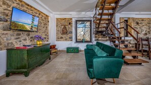 Ein Wohnzimmer mit einer Steinwand, einem grünen Sofa, einer Holztreppe und einem an der Wand befestigten Fernseher.