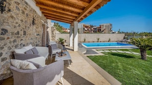 A covered outdoor area with stone walls, a pool, and a grassy lawn.