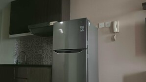 A compact kitchen with a stainless steel refrigerator, a wooden cabinet, and a tiled backsplash. - EXPRESS O 92140 Appartel (Bekasi)