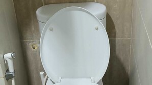 A white toilet in a bathroom with beige tiles. - EXPRESS O 92140 Appartel (Bekasi)