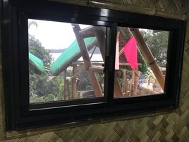 A window with a view of a wooden structure with a green roof and a pink flag.