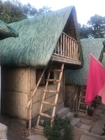 A traditional bamboo structure with a thatched roof and a wooden staircase leading to a balcony.