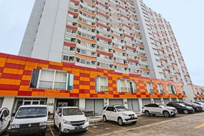 Un immeuble résidentiel à plusieurs étages, doté de balcons et d’un espace de stationnement à l’avant.