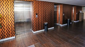 A hallway with patterned walls, an elevator, and a trash bin. - OYO 92317 Apartment Riverview By Alima View (Cikarang)