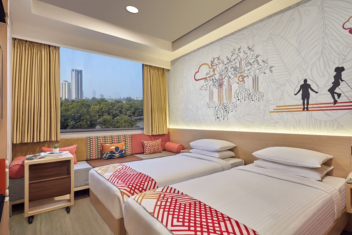 A hotel room with two beds, a sofa, a nightstand, and a large window with a city view.