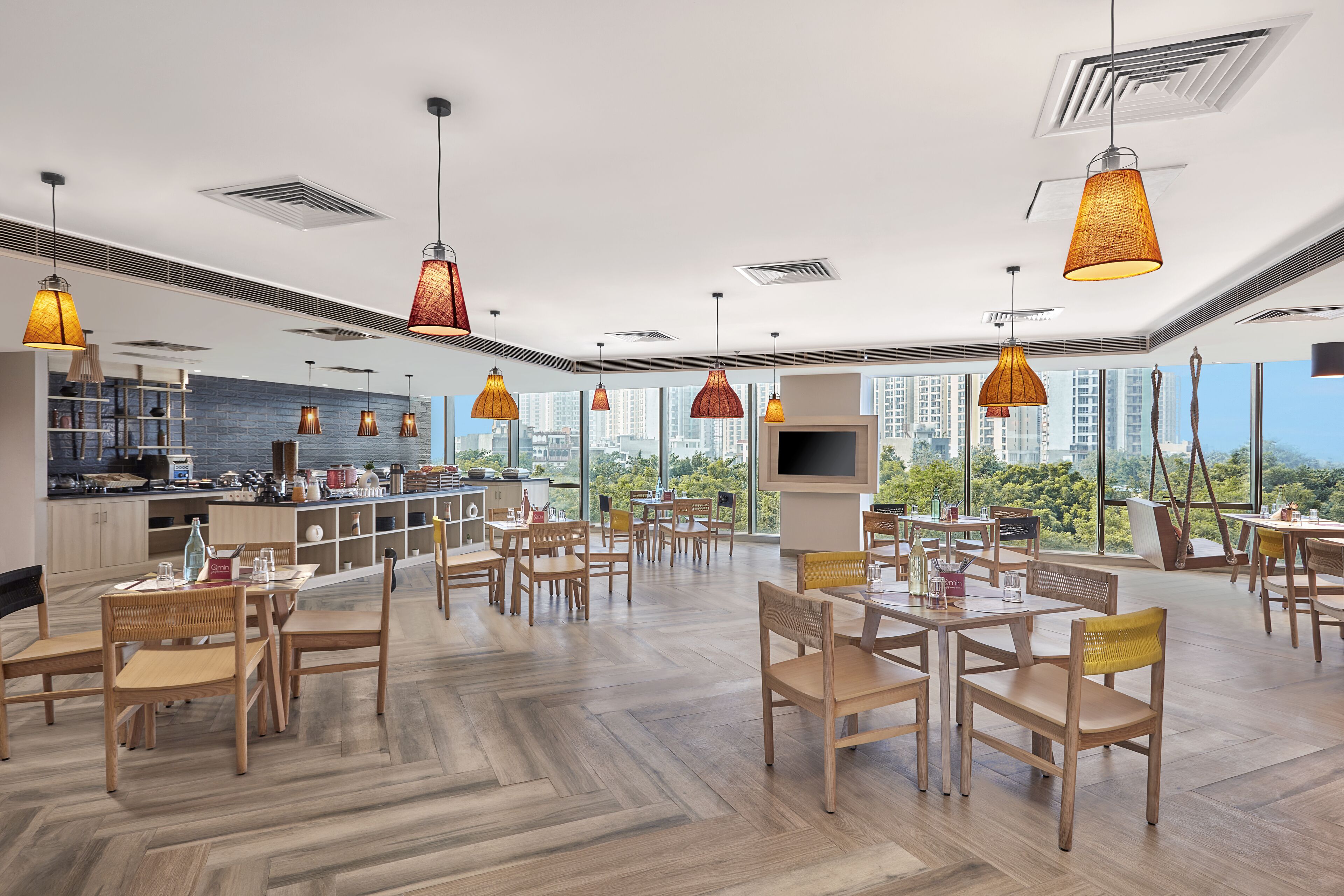 Un vaste espace de salle à manger avec des tables et des chaises en bois, de grandes fenêtres donnant sur la ville et un éclairage suspendu.