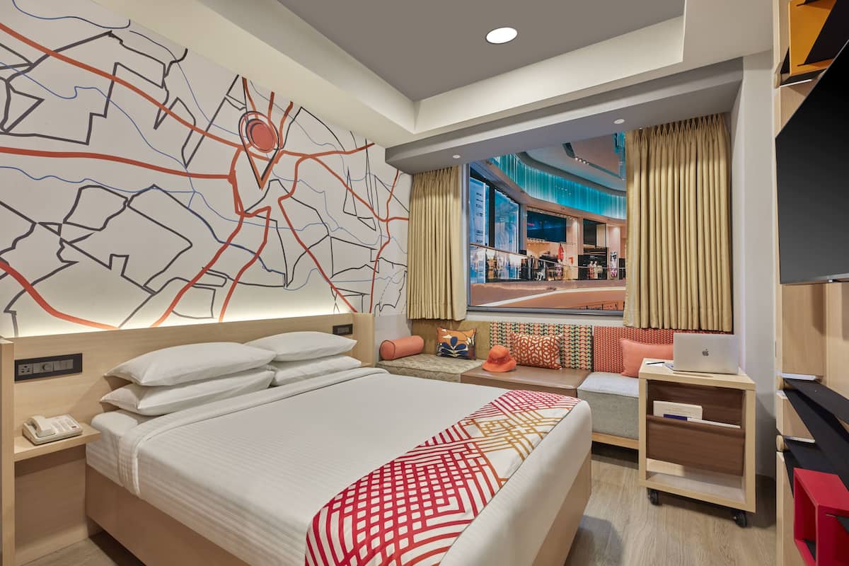 A modern hotel room with a large bed, a desk, a laptop, and a view of the cityscape.