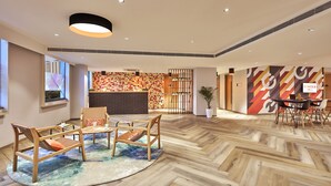 A spacious lobby with a wooden herringbone floor, a reception desk, and a dining area with a table and chairs. - Ginger Noida Sector 133 (Noida)