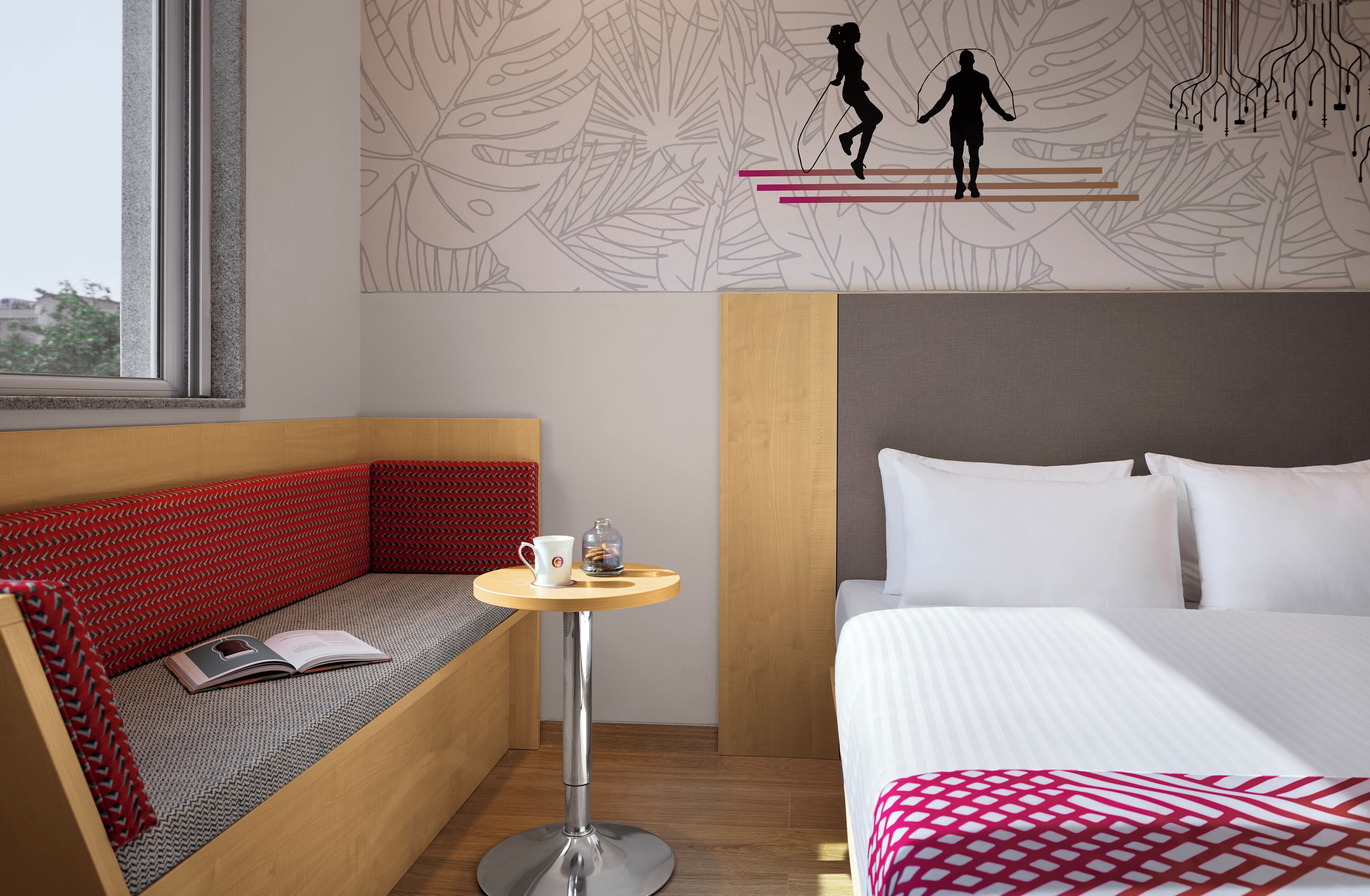 A hotel room with a bed, a seating area with a table, and a wall with a leaf pattern.