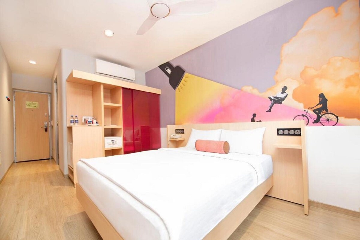A hotel room with a bed, a desk, a wardrobe, and a mural on the wall.