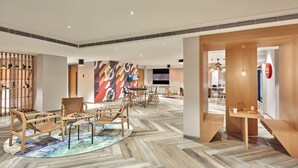 A spacious lobby with a herringbone patterned floor, wooden furniture, and a large abstract mural on the wall. - Ginger Noida Sector 133 (Noida)