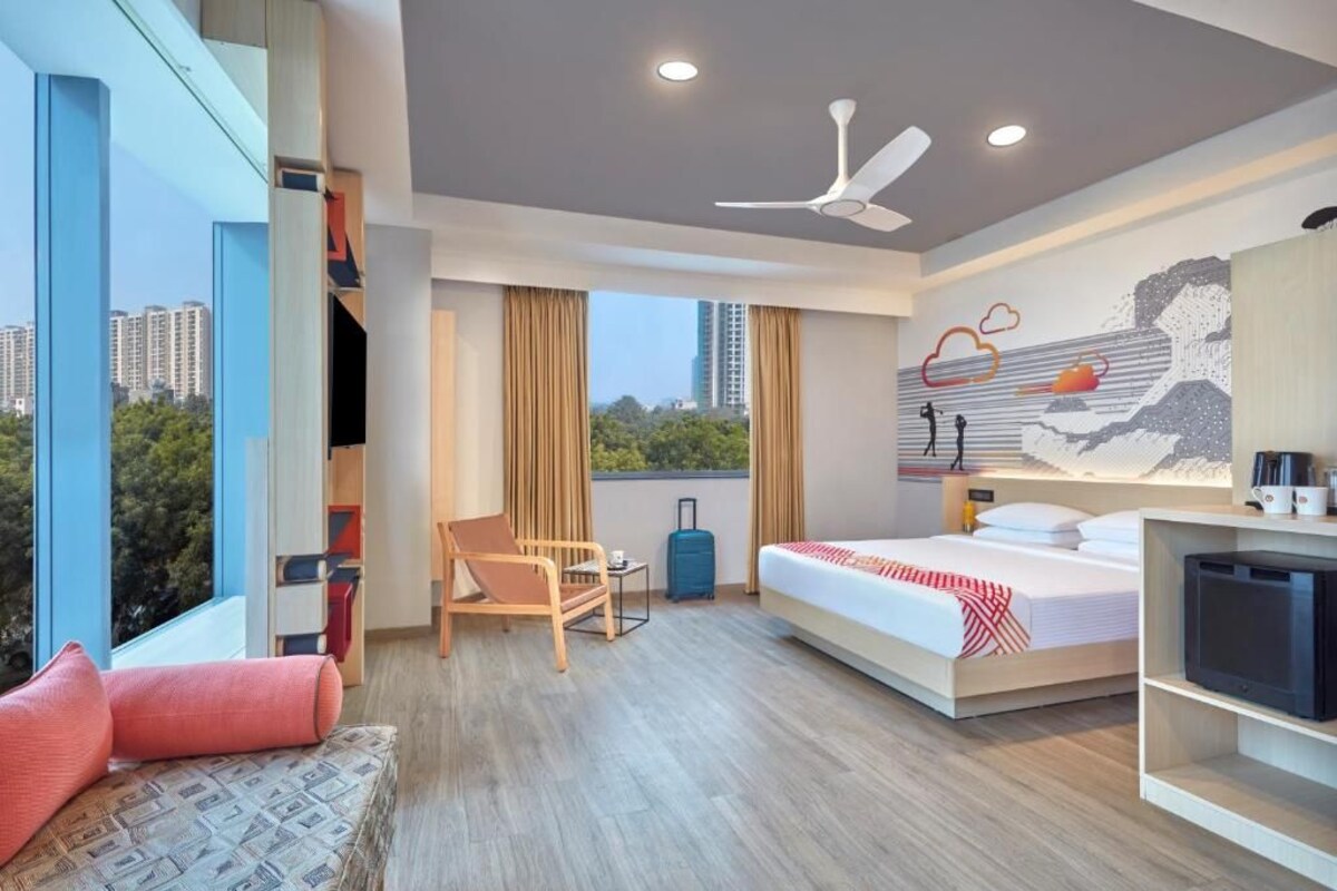 Une chambre d’hôtel moderne équipée d’un lit, d’un canapé, d’un bureau, d’un ventilateur de plafond et d’une grande fenêtre donnant sur la ville.