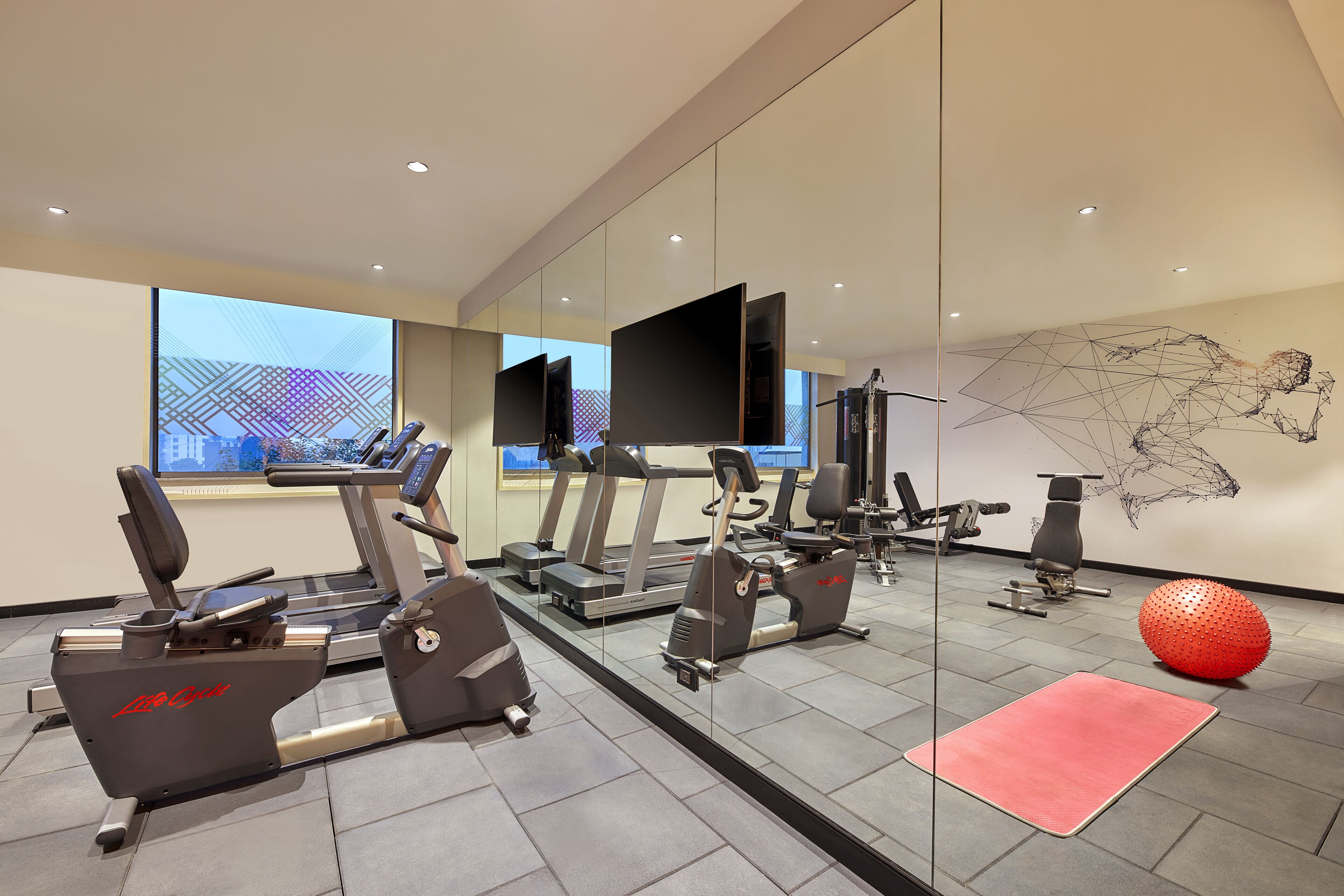Een moderne sportschool met cardioapparatuur, een rode fitnessbal en een grote spiegel die de ruimte weerspiegelt.