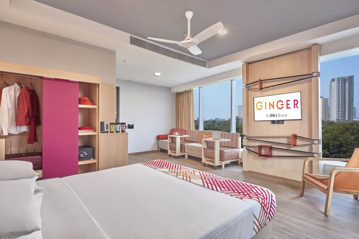 A modern hotel room with a large bed, a seating area with a sofa and chairs, a wardrobe, and a city view.
