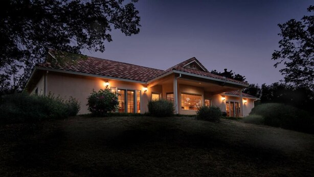 A two-story house with a covered porch, large windows, and a well-lit exterior at dusk. - Guinda's Finest Nature Get-Away! (Guinda)