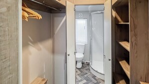 En rymlig klädkammare med hyllor i trä, en klädstång och en duschhörna med en vit toalett.