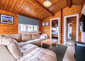 A log cabin interior with a leather sofa, a wooden table, a TV, and a bunk bed.