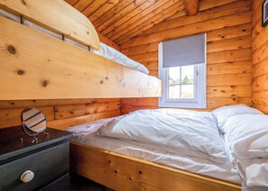 Una habitación de cabaña de madera con una litera, una mesita de noche con espejo y una ventana con vistas.