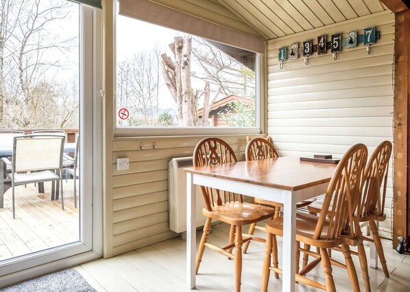 Un comedor con una mesa y sillas de madera, una ventana que ofrece vistas a árboles, y una pared con ganchos numerados.