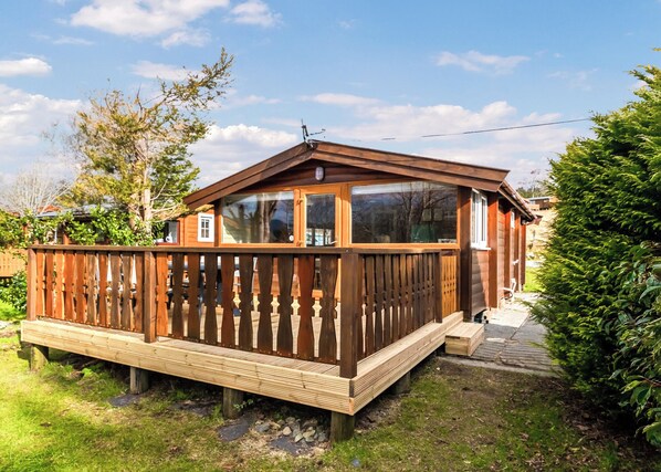 Une cabane en bois dotée d’une terrasse, de grandes fenêtres et d’une cheminée.