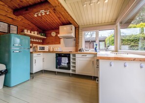 Une cuisine avec des poutres en bois au plafond, des meubles blancs, un réfrigérateur de couleur turquoise et une fenêtre donnant sur un paysage verdoyant.