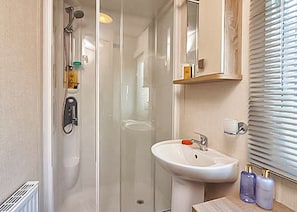 Un baño con cabina de ducha de vidrio, lavamanos pedestal y espejo sobre el lavamanos.