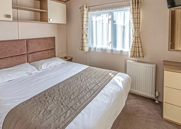 Ein Schlafzimmer mit Bett, Nachttisch, Kommode, Heizkörper und einem Fenster mit Vorhängen.