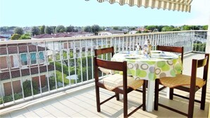 Een balkon met een tafel en stoelen, uitzicht op gebouwen en een hekwerk.