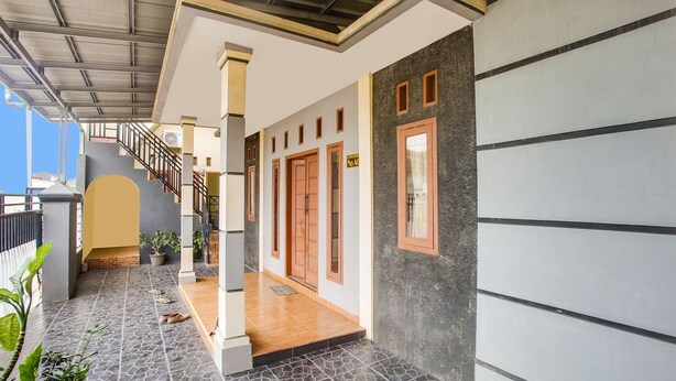 A covered outdoor area with a staircase leading to a second floor, potted plants, and a tiled floor. - OYO Life 3005 Kost Rumaisha Syariah (Bandar Lampung)