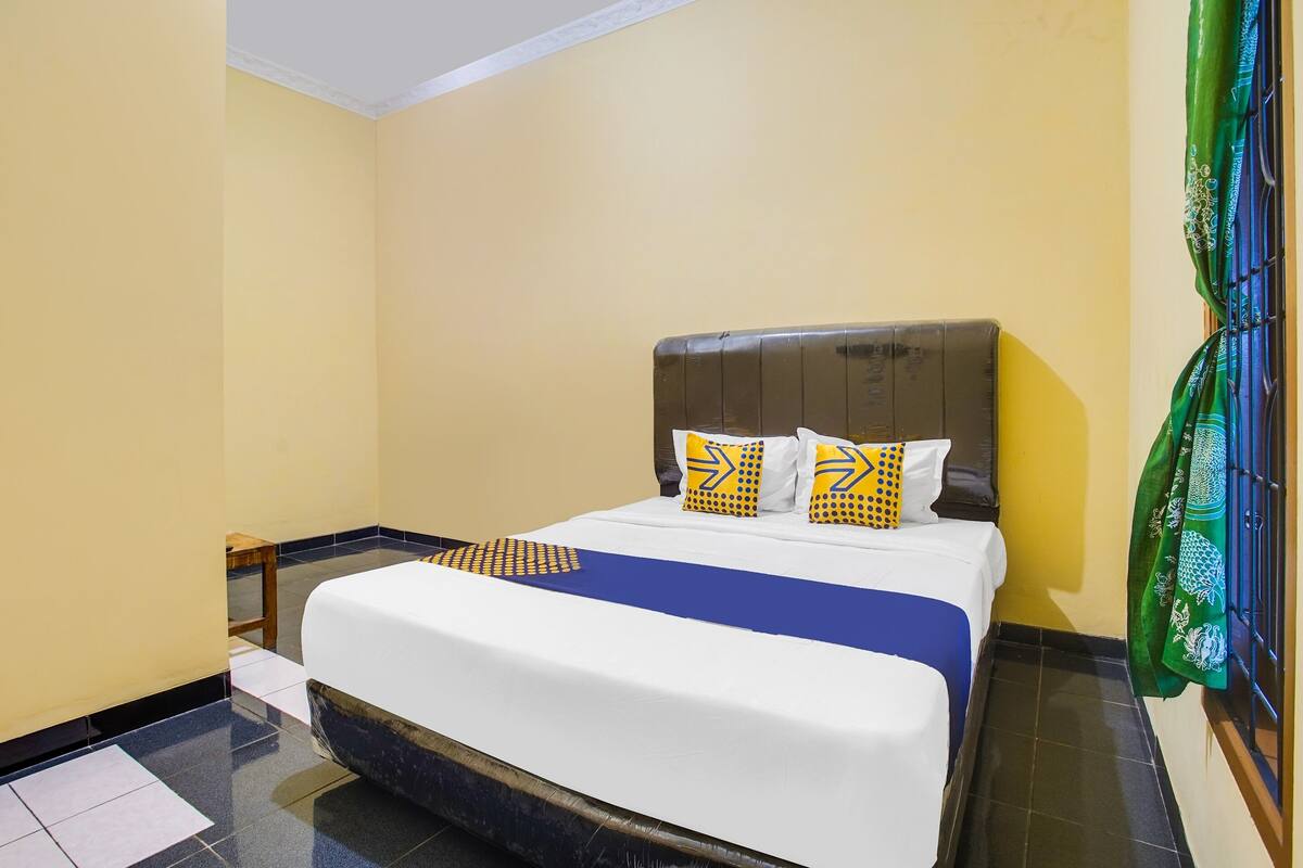 A hotel room with a large bed, a wooden nightstand, and a green curtain.
