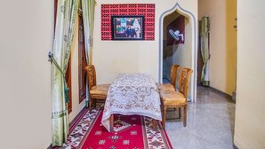 A dining area with a table covered by a white tablecloth, two wooden chairs, and a patterned red carpet. - OYO Life 3005 Kost Rumaisha Syariah (Bandar Lampung)