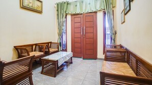 A room with a wooden dining table and chairs, a large window with curtains, and a door with a traditional design. - OYO Life 3005 Kost Rumaisha Syariah (Bandar Lampung)