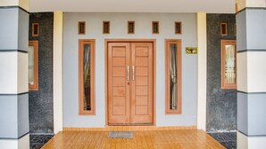 A front view of a building with a central double wooden door, flanked by windows with curtains, and a sign indicating a price of 40. - OYO Life 3005 Kost Rumaisha Syariah (Bandar Lampung)