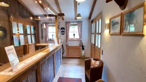 Un hall d’hôtel accueillant, avec un comptoir de réception en bois, un paillasson rouge, un banc en bois et une fenêtre avec des rideaux.