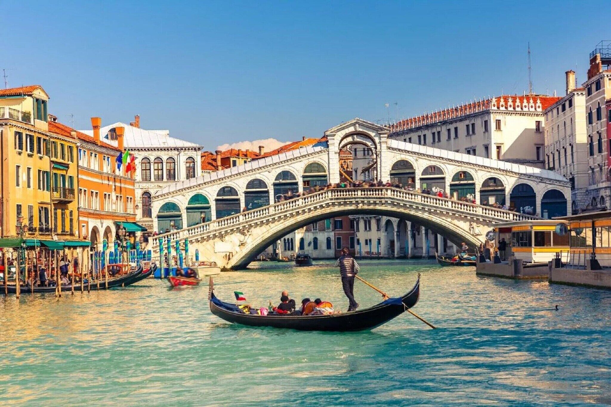 A historic bridge with arches, gondolas, and buildings along a canal.