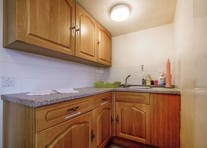 Eine Küche mit Holzschränken, einer Granitarbeitsplatte und einem Spülbecken mit Spülmittel und einer Zahnbürstenhalterung.
