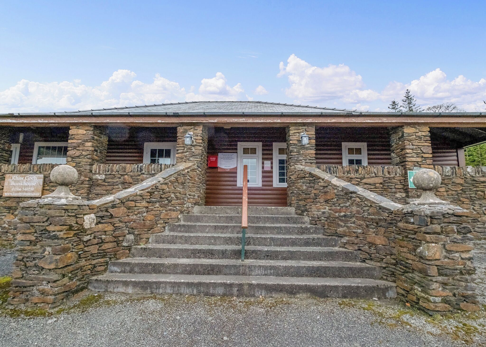 A stone building with a wooden exterior, a set of stone steps leading to a door, and a signboard.