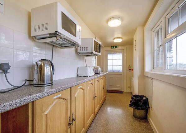 A kitchen with a microwave, toaster, kettle, and a trash bin.