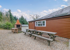 Une cabane en bois avec une cheminée, une fenêtre et une table de pique-nique.